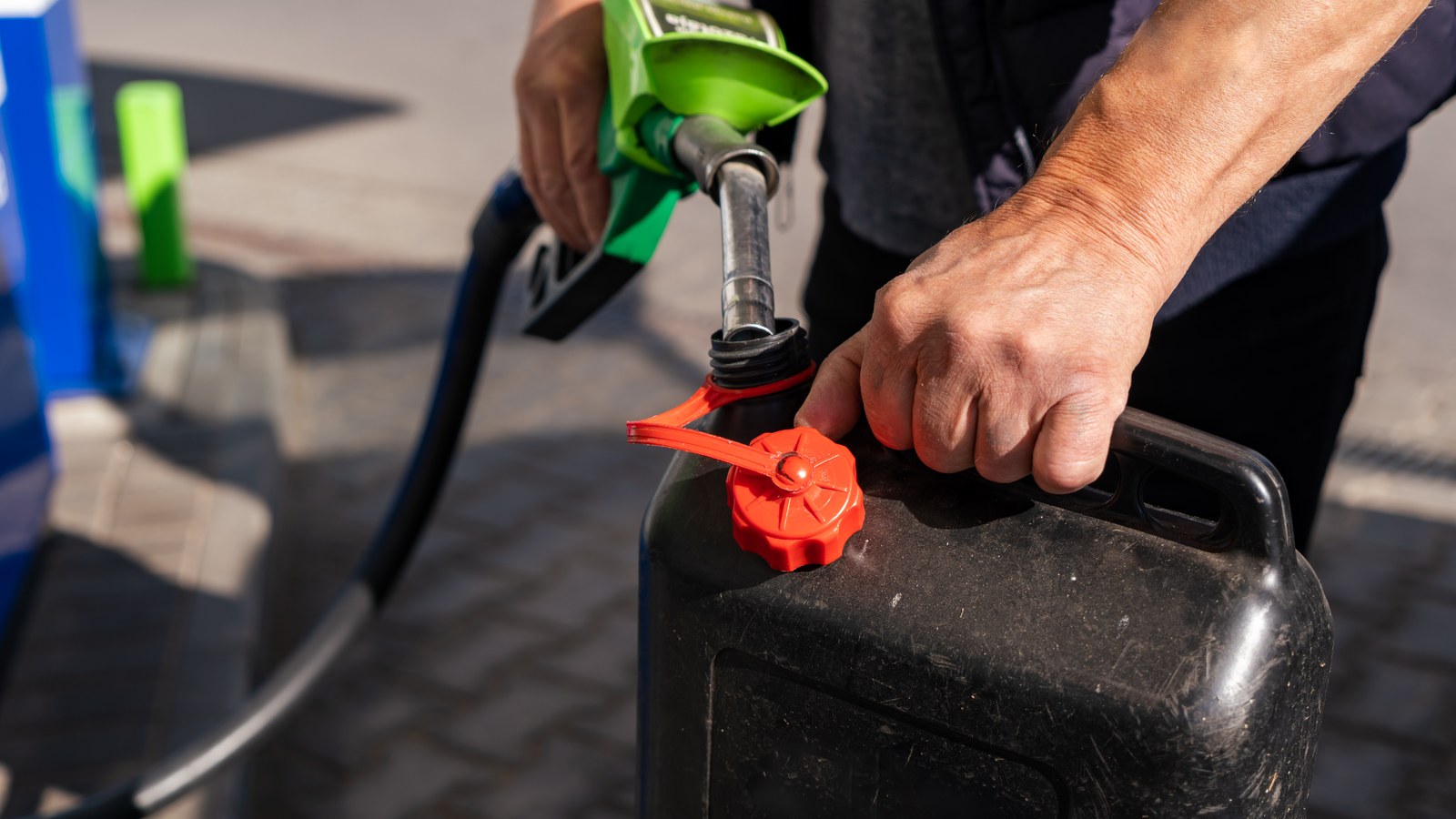 A person fills a fuel canister at a petrol station pump