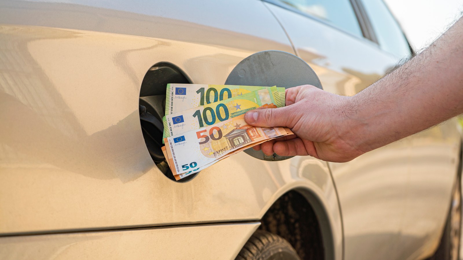 Hand pushing euro banknotes into a car's fuel filler